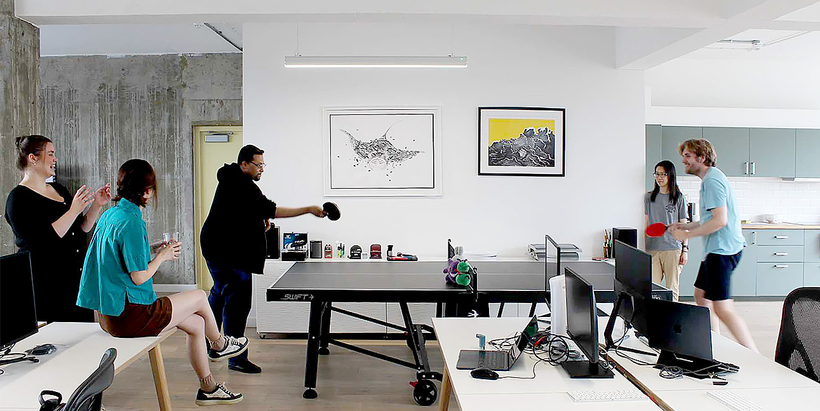 Image of an office social event featuring employees playing ping pong, with colleagues enjoying the game and interacting in a relaxed, fun environment.